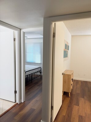 Een kamer met een bed, houten vloeren, een witte deur en een klein houten kastje.