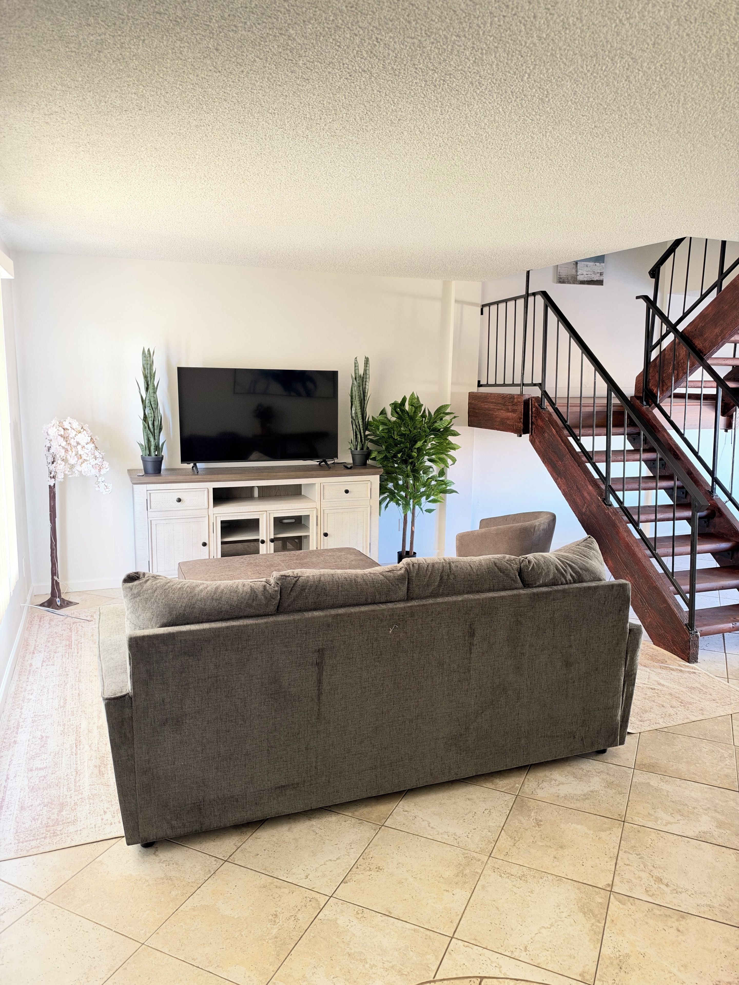 A living room with a sofa, a flat-screen TV, a staircase, and a potted plant.