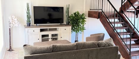A living room with a sofa, a flat-screen TV, a staircase, and a potted plant.