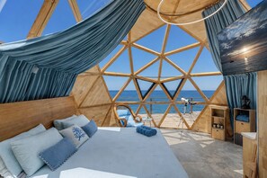 A room with a geometric wooden structure, a bed with blue bedding, a telescope, and a view of the sea. - Villa & dômes : 8 bdr - Breathtaking 180° views - Beach Access & Pickle ball (Les Terres Basses)