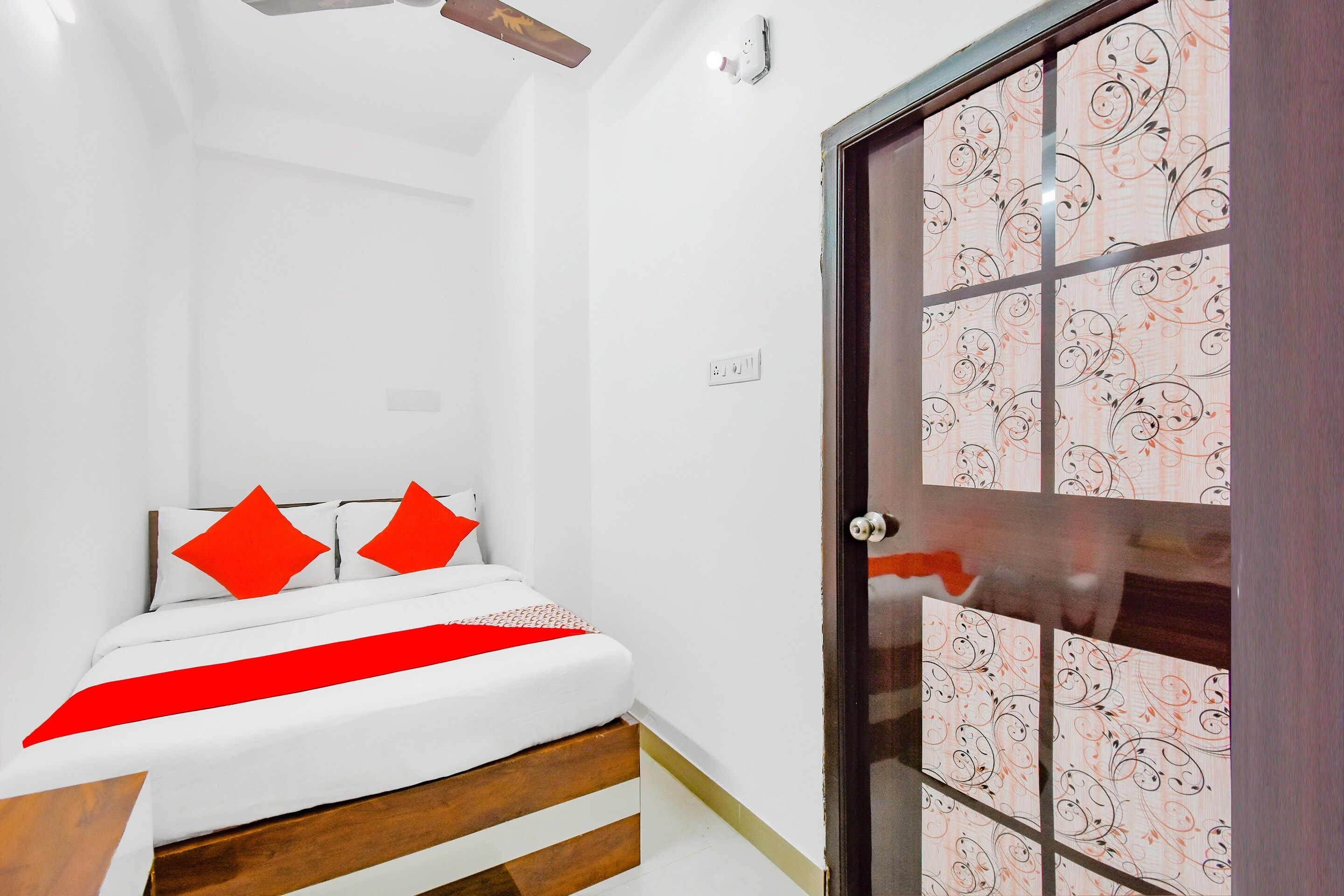 Een slaapkamer met een bed, een houten hoofdbord, een rood-witte dekbedovertrek en een deur met een patroon.