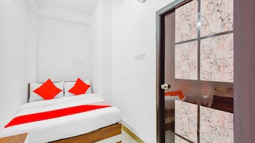 Een slaapkamer met een bed, een houten hoofdbord, een rood-witte dekbedovertrek en een deur met een patroon.