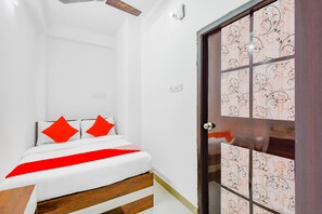 A bedroom with a bed, a wooden headboard, a red and white bedspread, and a patterned door. - Hotel O Royal Palace (Barasat)