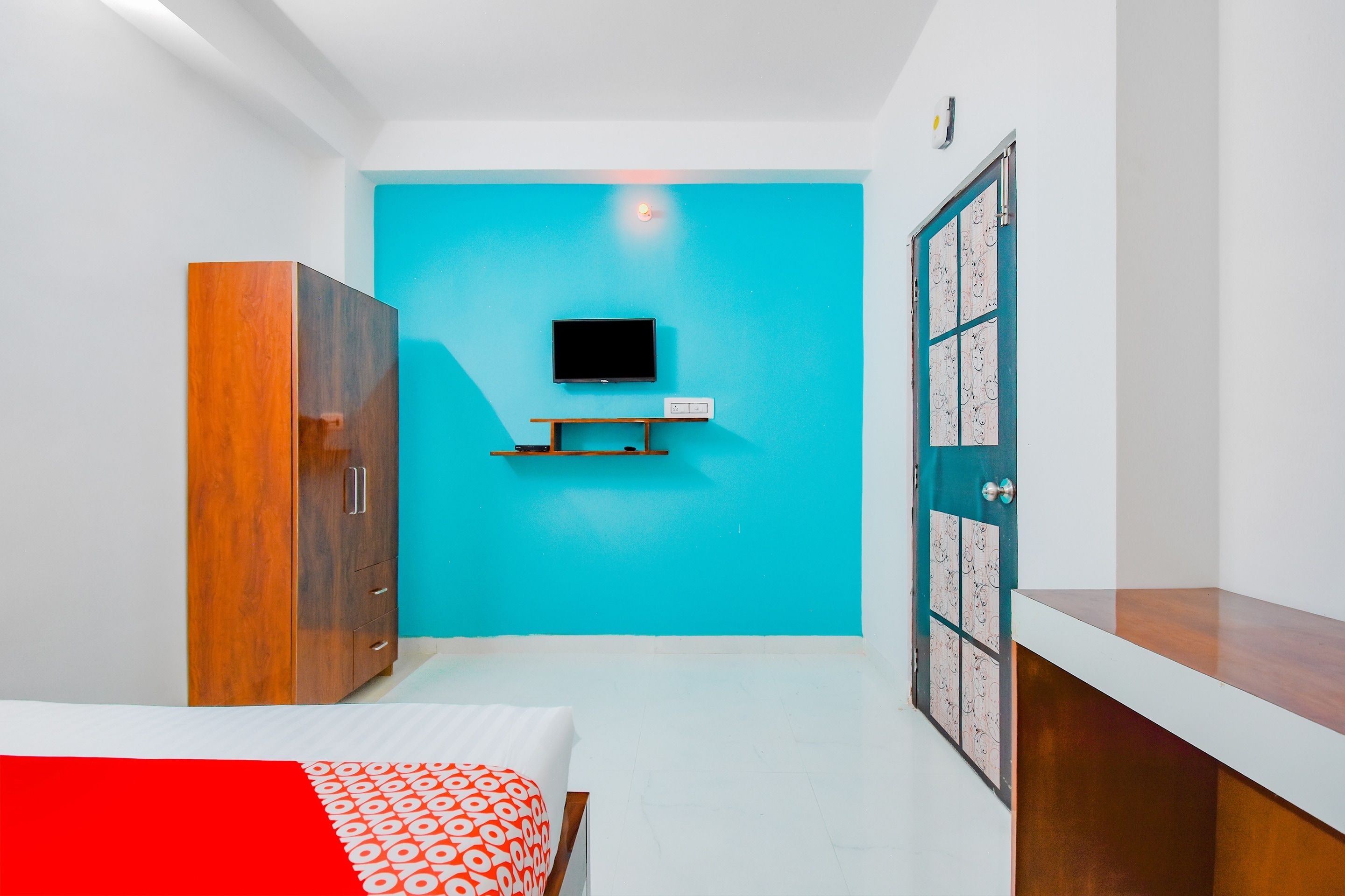 Un dormitorio con cama, armario, televisor montado en la pared y una puerta con diseño decorativo.