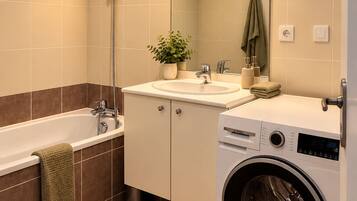 Une salle de bain moderne équipée d’une baignoire, d’une douche, d’un lavabo et d’un lave-linge à chargement frontal.