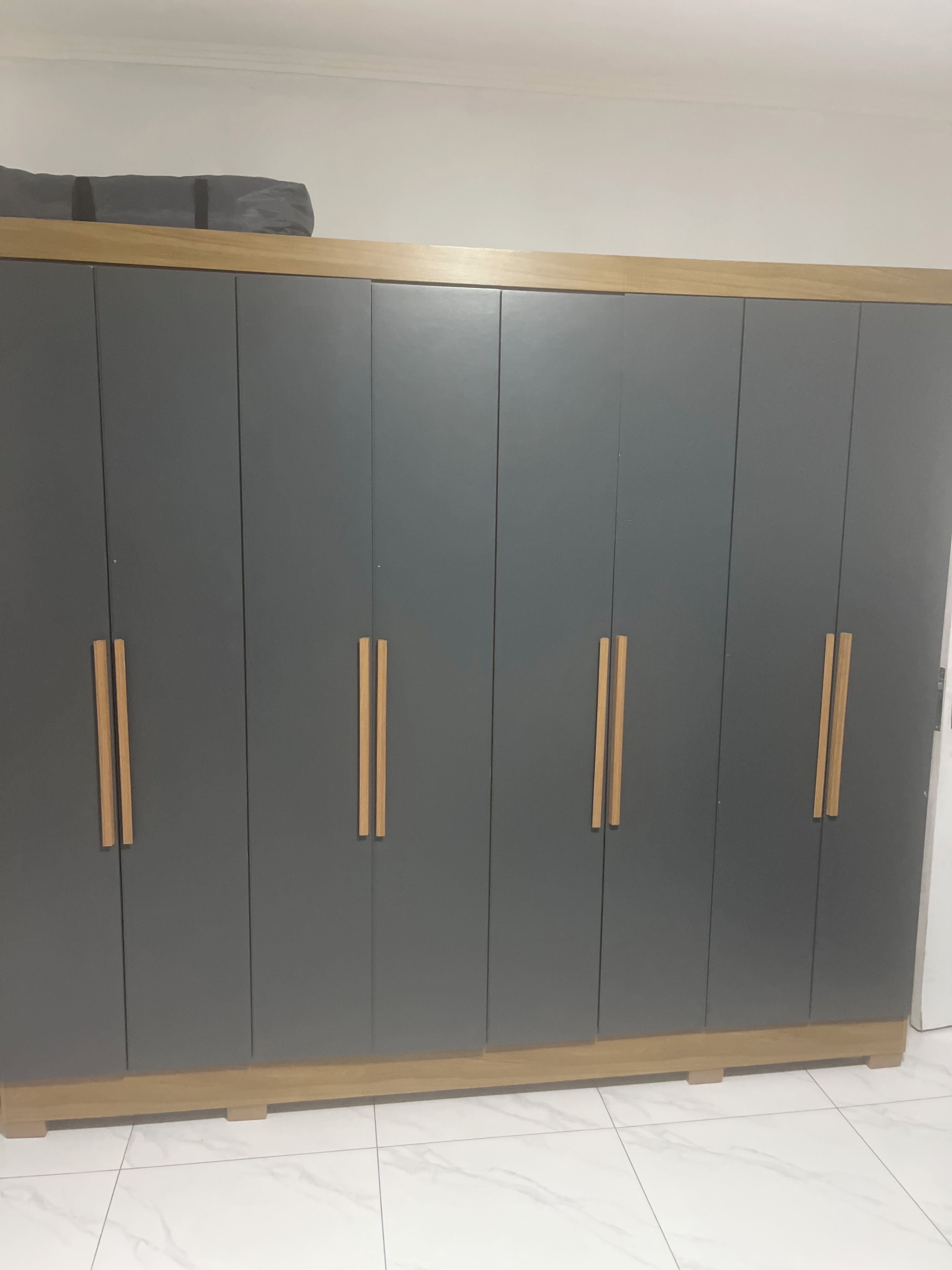 A large grey wardrobe with wooden handles and a wooden baseboard.