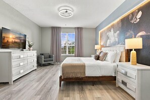 Ein modernes Schlafzimmer mit Bett, Nachttischen, Fernseher und einem großen Fenster.