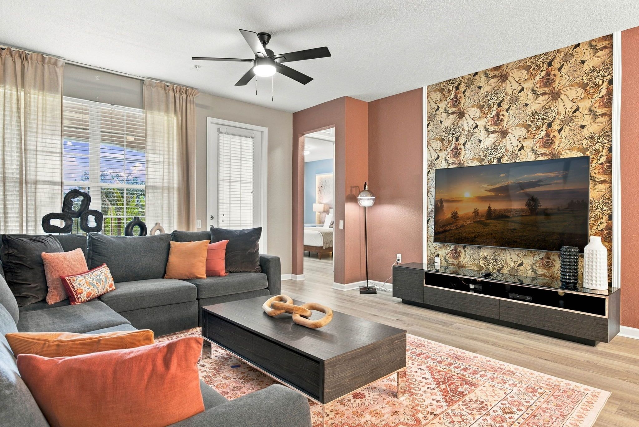 A modern living room with a sofa, coffee table, and a flat-screen TV mounted on a wall with a floral wallpaper.