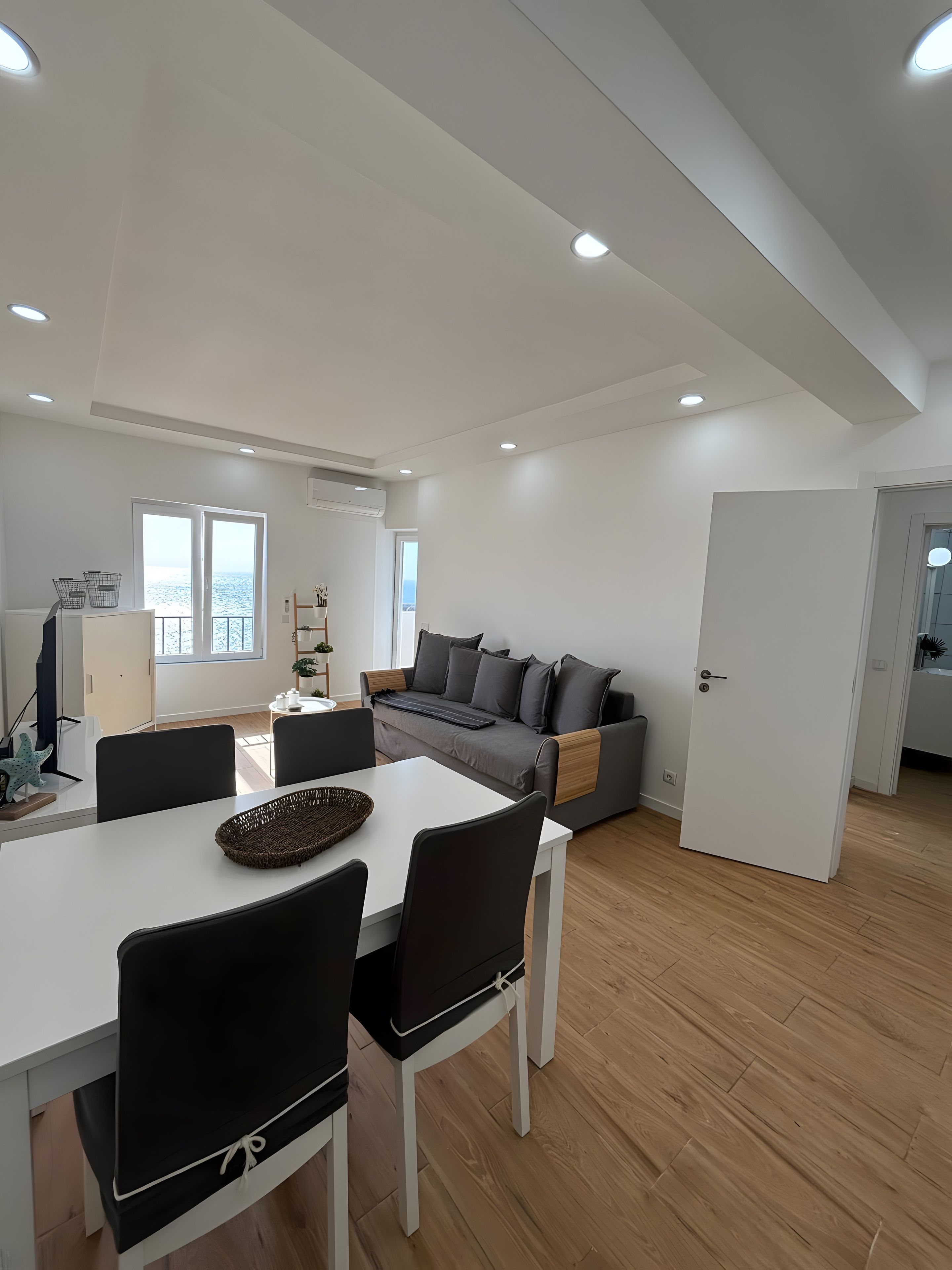 A modern living room with a dining area, a sofa, and a view of the sea.