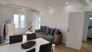A modern living room with a dining area, a sofa, and a view of the sea.