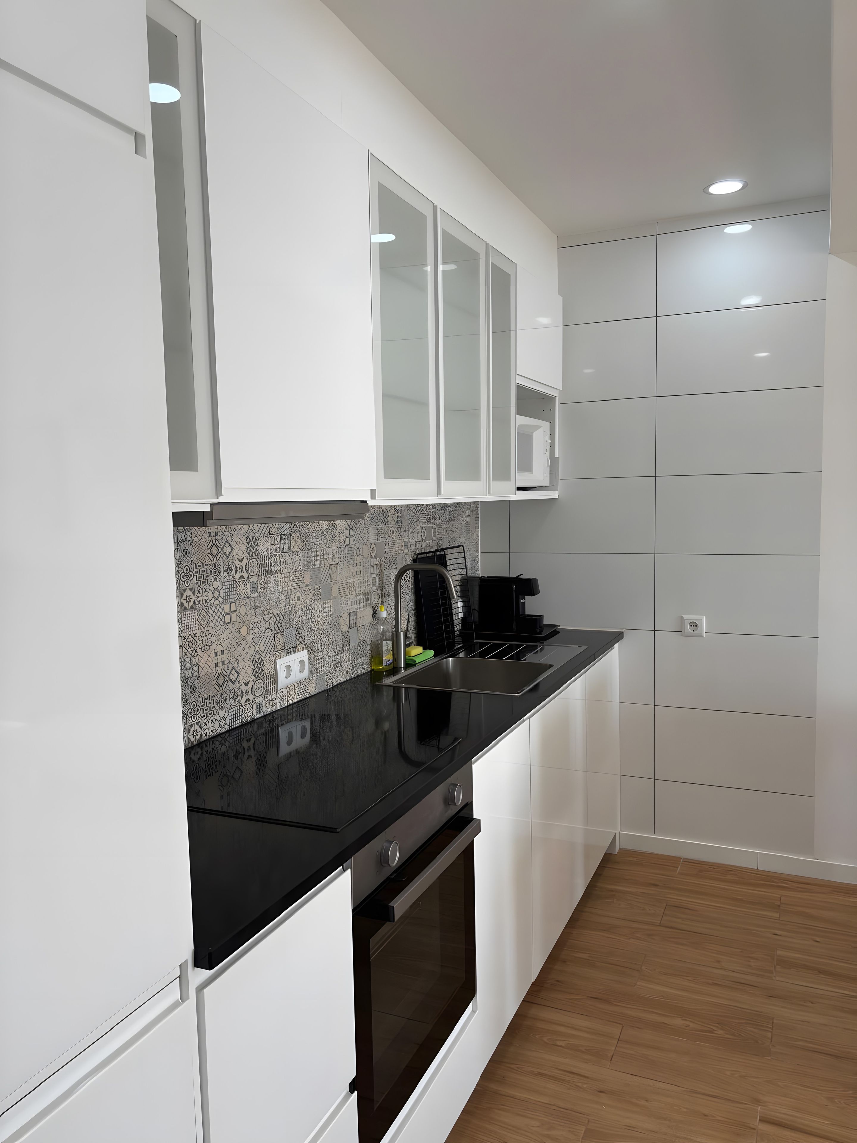 A modern kitchen with white cabinetry, a black countertop, and a patterned backsplash.