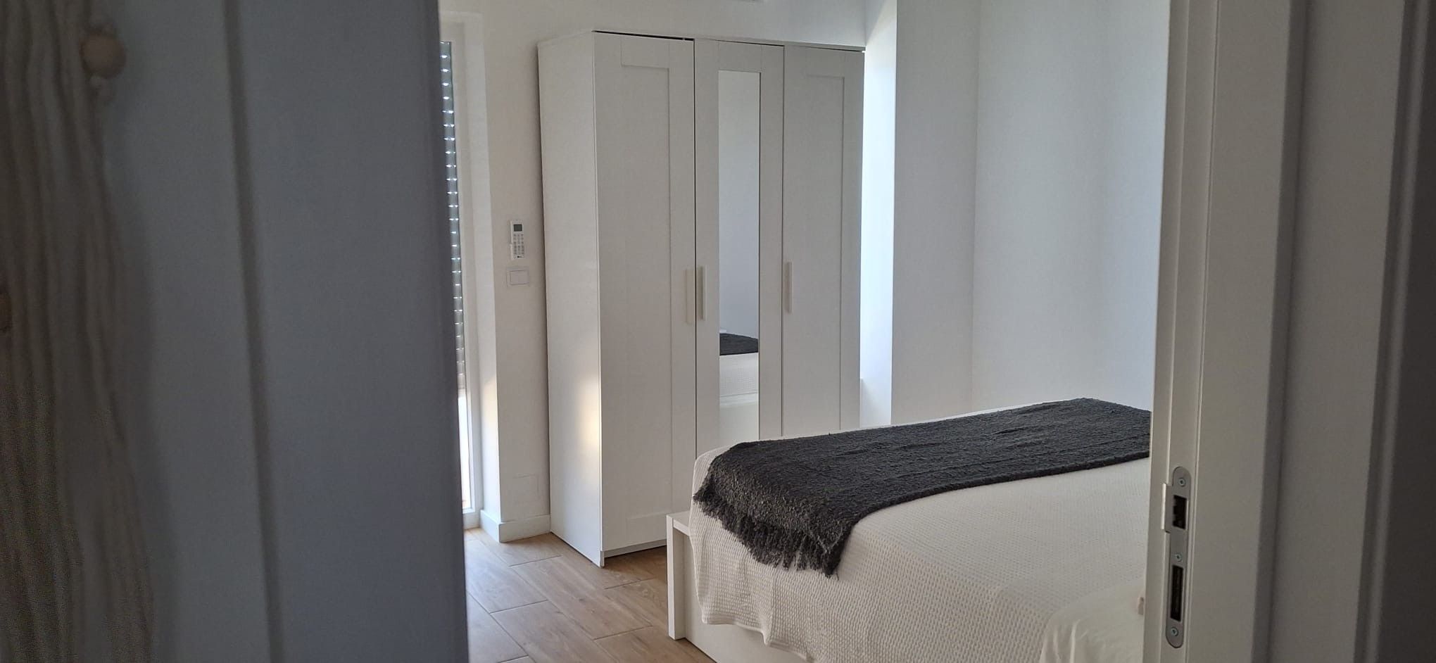 A bedroom with a bed, a wardrobe, and a door leading to another room.