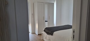 A bedroom with a bed, a wardrobe, and a door leading to another room. - Holiday Home 'Modern and Sunny, Sea View' with Wi-Fi and Air Conditioning (Quarteira)