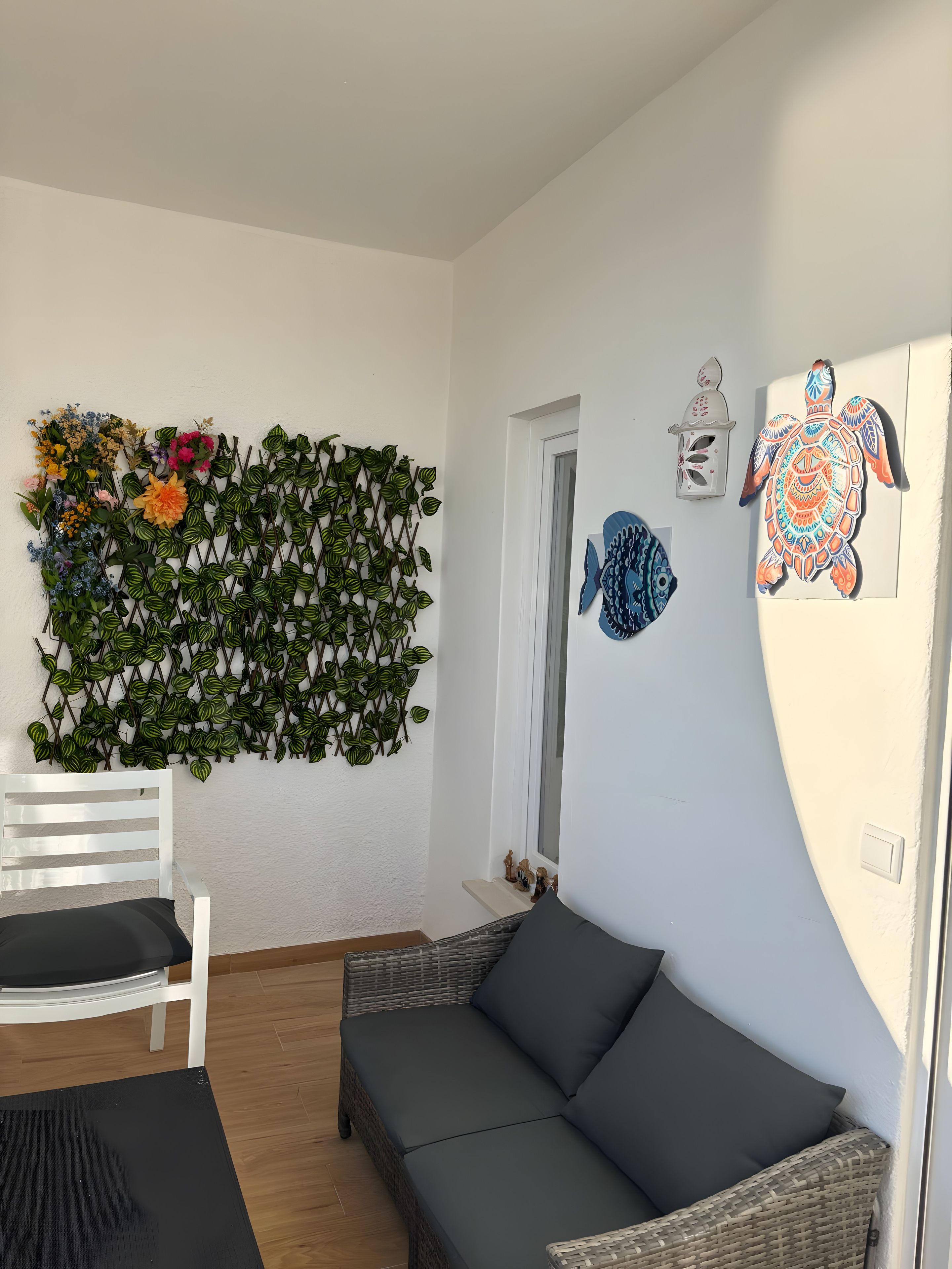 Une pièce avec un mur blanc, une décoration murale, une chaise blanche, un canapé gris foncé et une petite étagère avec des figurines.