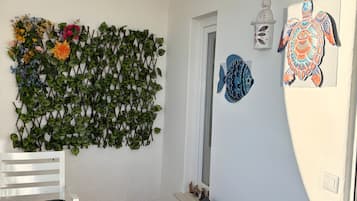 Une pièce avec un mur blanc, une décoration murale, une chaise blanche, un canapé gris foncé et une petite étagère avec des figurines.