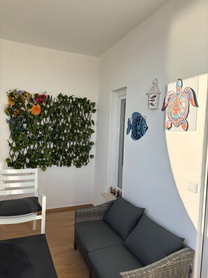 A room with a white wall, a decorative wall hanging, a white chair, a dark grey sofa, and a small shelf with figurines. - Holiday Home 'Modern and Sunny, Sea View' with Wi-Fi and Air Conditioning (Quarteira)