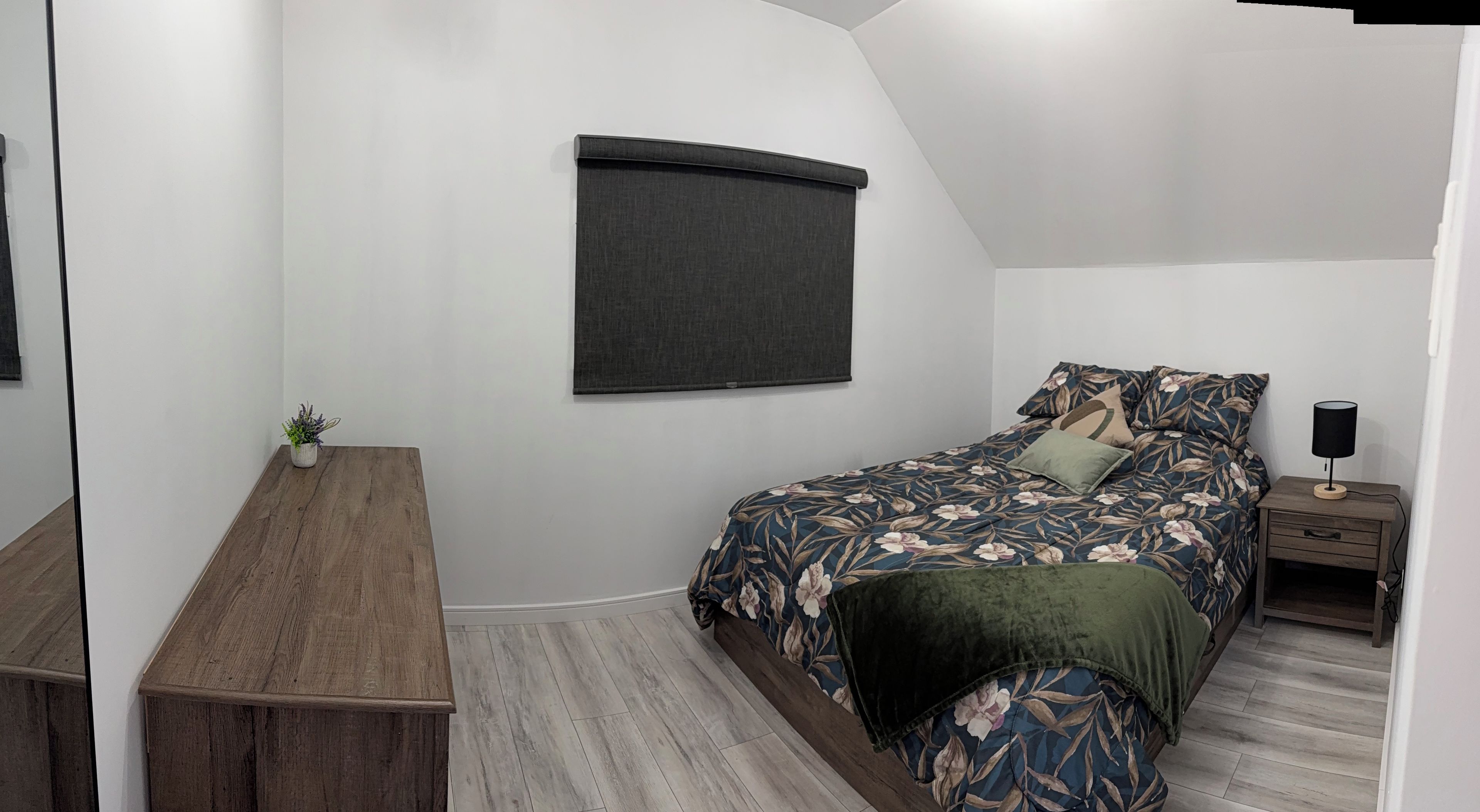 Un dormitorio con cama, mesita de noche, lámpara y ventana con persiana.