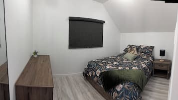 Un dormitorio con cama, mesita de noche, lámpara y ventana con persiana.