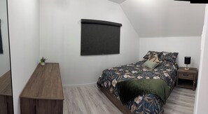 Ein Schlafzimmer mit Bett, Nachttisch, Lampe und einem Fenster mit Jalousie.