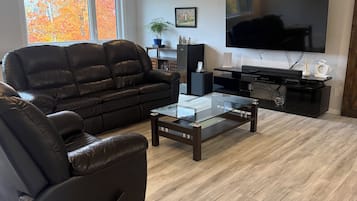 Una sala de estar moderna con un sofá de cuero, una mesa de centro de vidrio, un televisor de pantalla plana y piso de madera.
