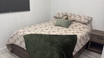 A bedroom with a bed, a nightstand, a window with a blind, and a wooden floor.