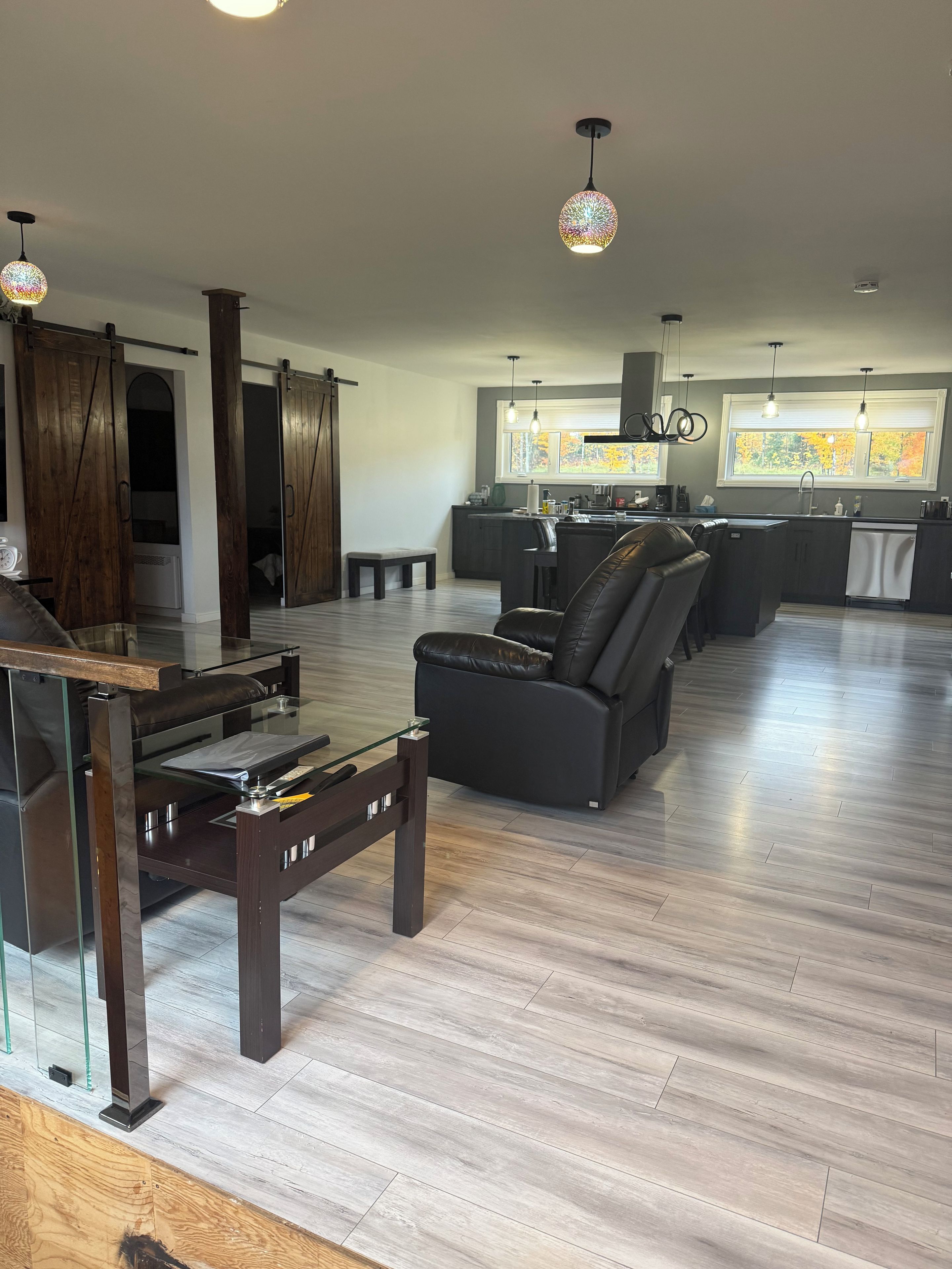 Een moderne woonkamer met een glazen salontafel, een zwarte bank en een keuken met een raam.