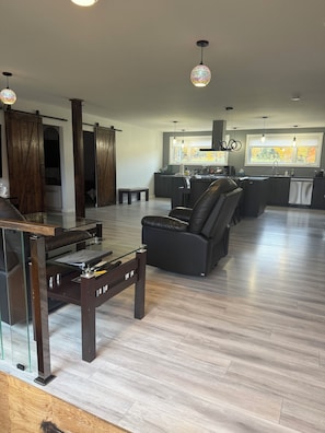 A modern living room with a glass coffee table, a black sofa, and a kitchen area with a window.