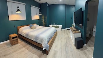 A modern bedroom with a wooden bed, bedside tables, a built-in bench, a white vanity, and a large flat-screen TV.