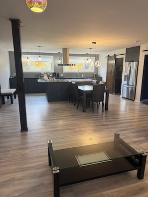 A modern kitchen with a central island, dining area, and a glass-top coffee table.