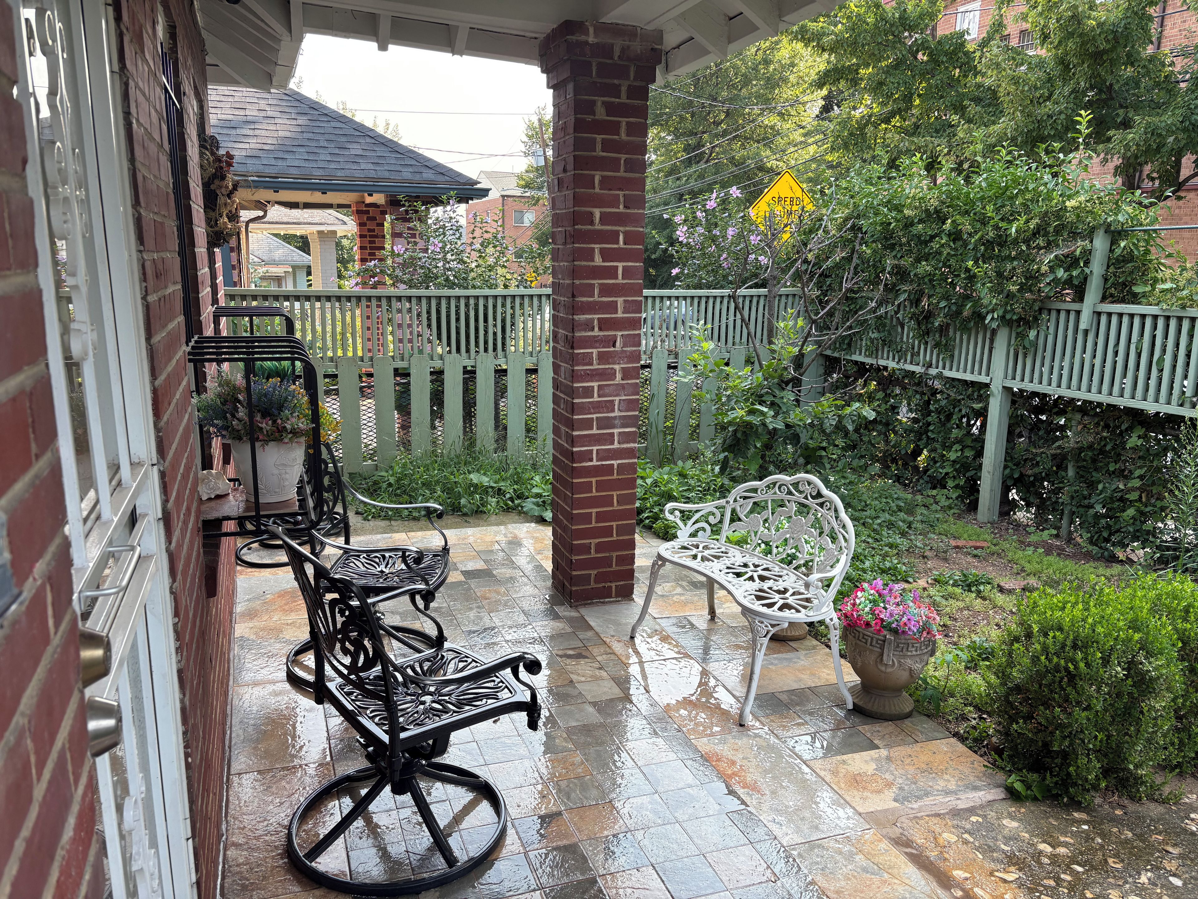 A covered patio with two white metal chairs and a black metal table.