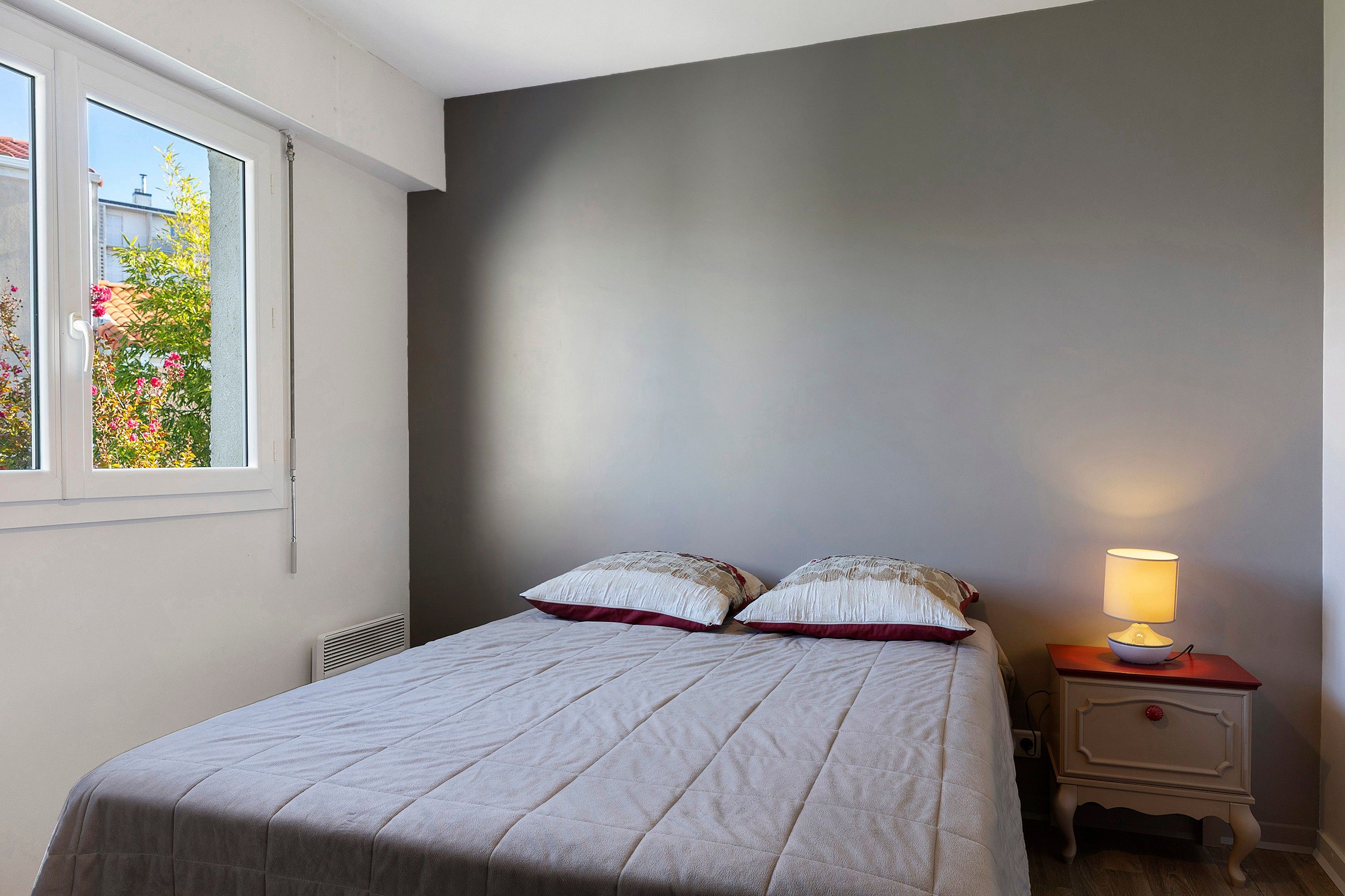 A bedroom with a bed, a nightstand, a lamp, and a window with a view of trees.