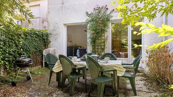 Eine Terrasse im Freien mit Esstisch, umgeben von Grünpflanzen und einem Grill.