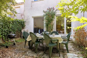 Eine Terrasse im Freien mit Esstisch, umgeben von Grünpflanzen und einem Grill.