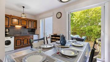 A dining area with a table set for four, a kitchen with wooden cabinets, and a view of a lush garden through a sliding glass door.
