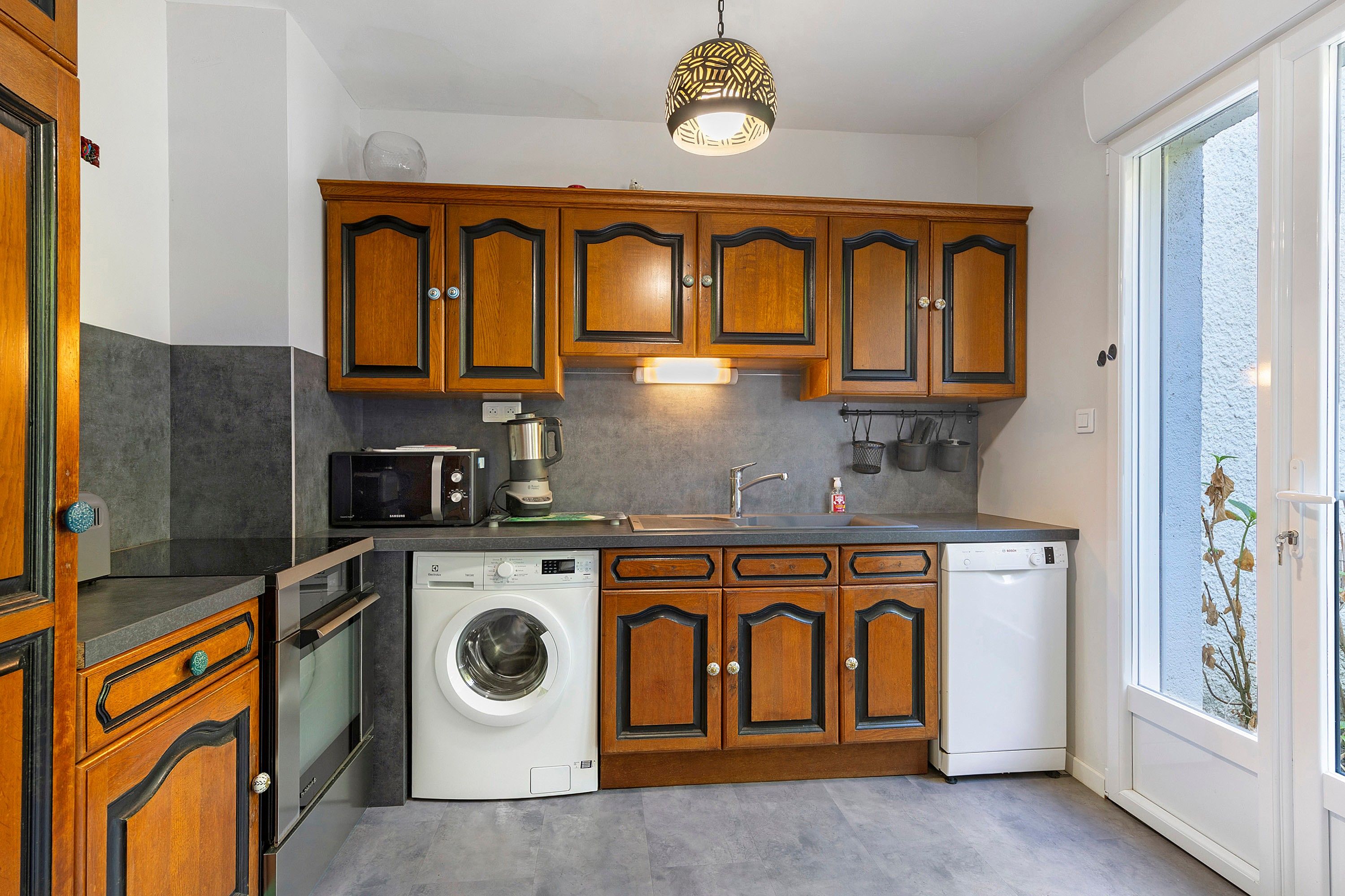 Une cuisine compacte avec des meubles en bois, un lave-linge, un four à micro-ondes et une machine à café.
