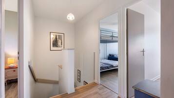 Een gang met een trap, een bed met een stapelbed, een nachtkastje met een lamp en een lijst met een afbeelding aan de muur.
