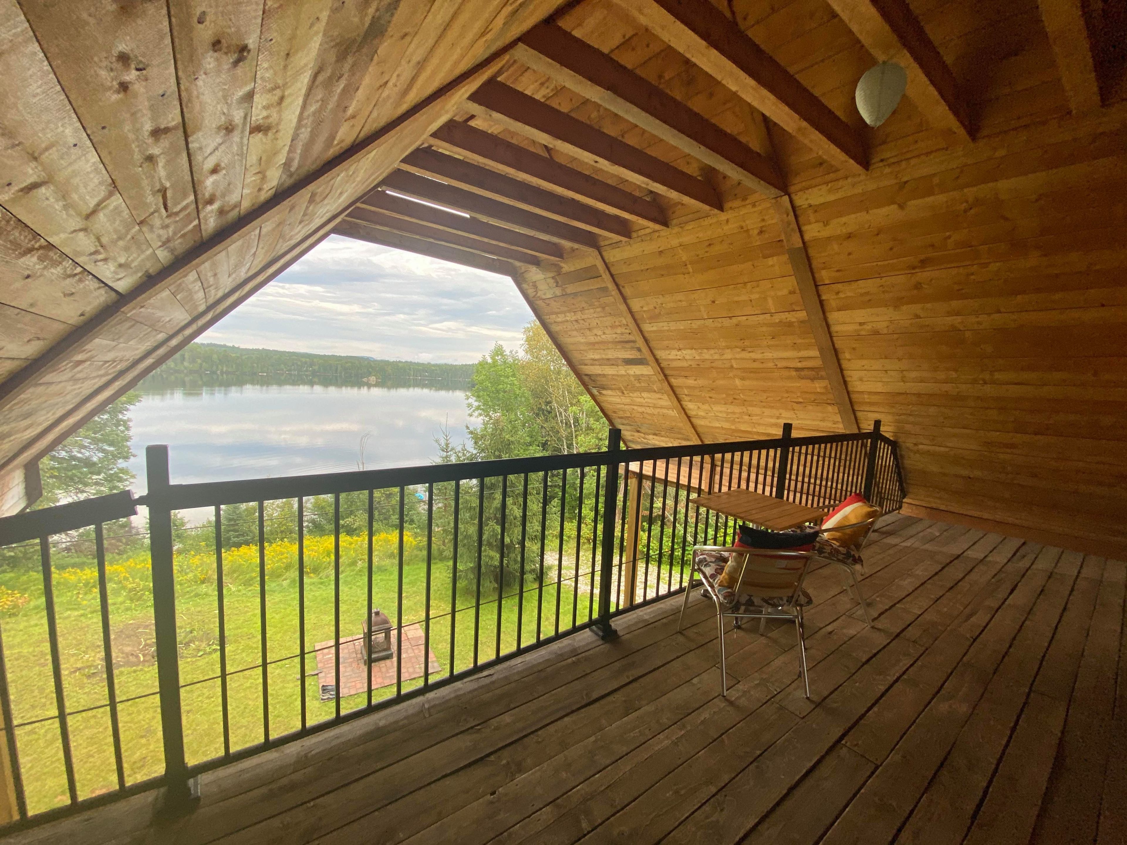 Una terraza de madera con vista a un lago, barandilla y una silla.