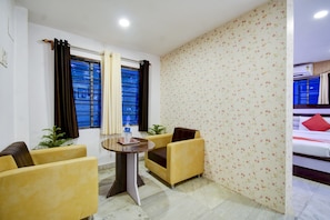 A hotel room with a bed, two yellow armchairs, a small round table with a bottle and glasses, and a window with blue bars. - Hotel O ROYAL REGENCY (Kolkata)