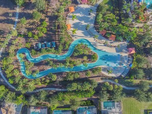 An aerial view of a resort with a winding pool, surrounded by palm trees and shaded areas. - Misty- 6 Bedroom/Htd Pool/Jacuzzi/Game Room/Water Park (Davenport)