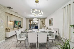 Un espace de salle à manger moderne avec une table et des chaises en verre, un lustre et une vue sur le salon.