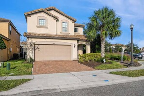 A two-story house with a garage, a paved driveway, and a well-maintained lawn with a palm tree. - Misty- 6 Bedroom/Htd Pool/Jacuzzi/Game Room/Water Park (Davenport)