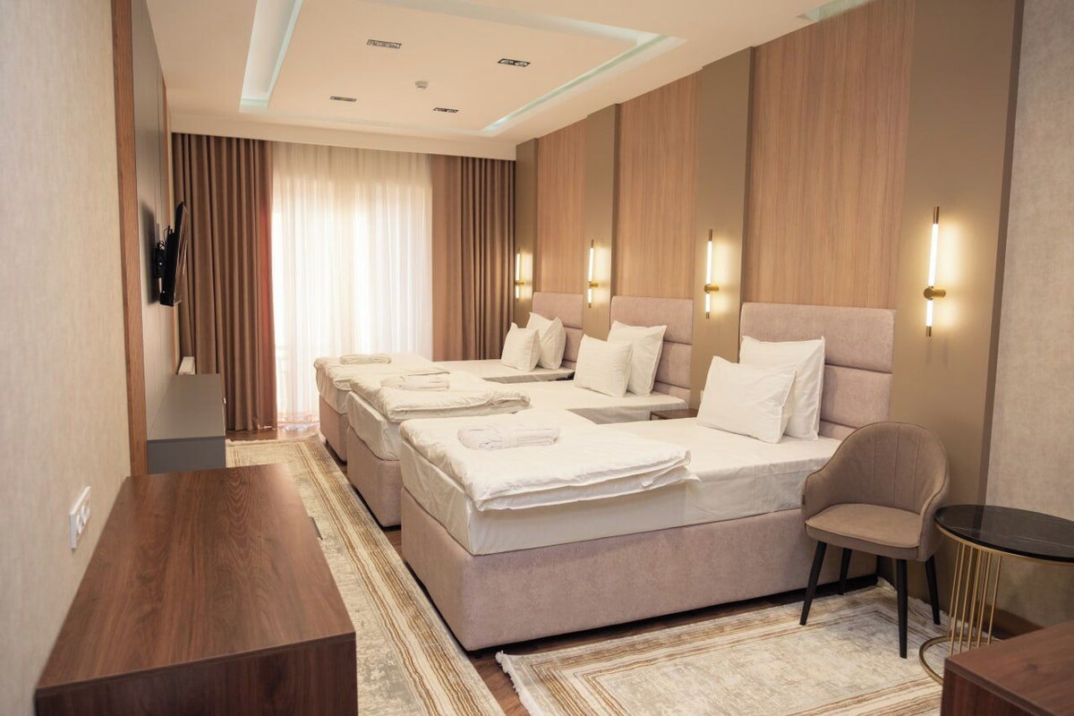 Quarto de hotel com uma cama grande, duas mesas de cabeceira, uma cadeira e televisão na parede.