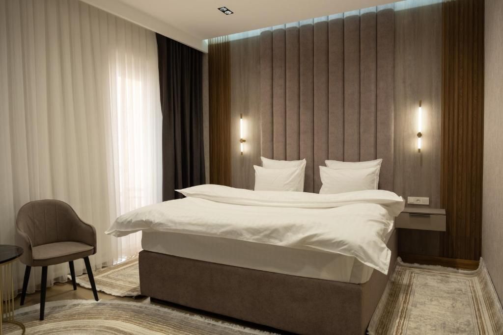 A modern hotel room with a large bed, a bedside table, a chair, and a wall-mounted light fixture.
