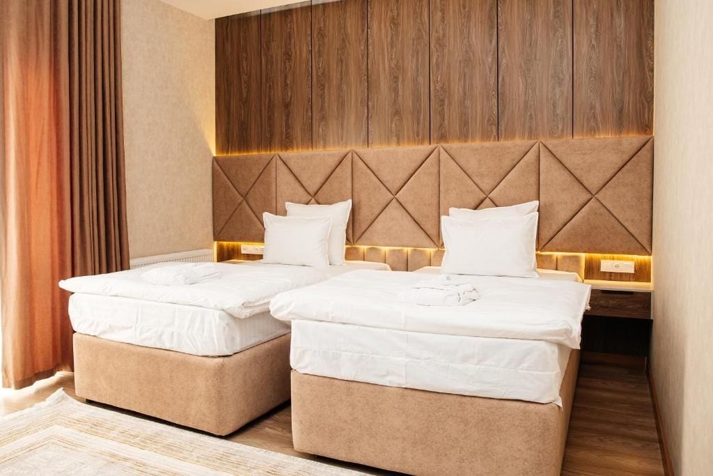 A hotel room with two beds, a wooden headboard, and a nightstand with a lamp.