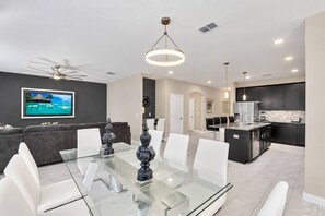 A modern kitchen with dark cabinets, a central island, and a dining area with a glass table and white chairs. - 6BR house with spa / jacuzzi near Disney (Davenport)