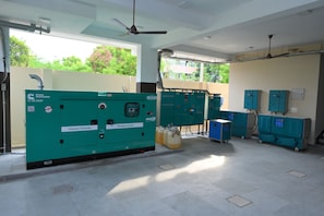 A clean, well-lit industrial space with large green electrical panels, ceiling fans, and a view of greenery outside. - DD Home2 Suites (Tiruchirappalli)