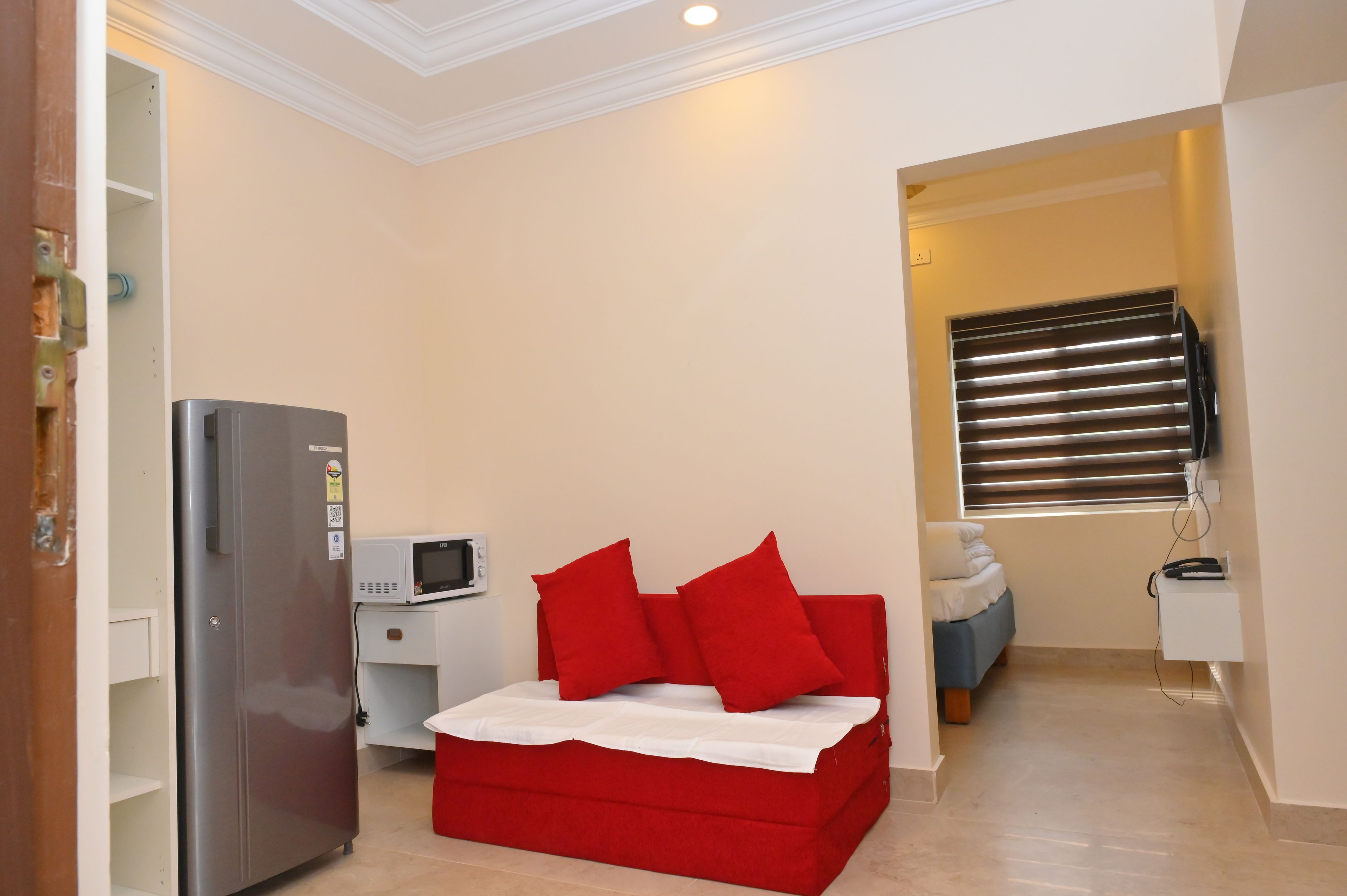 Habitación compacta con cama, refrigerador, microondas y ventana con persianas.