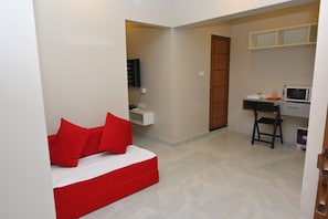 Ein kleines Zimmer mit Bett, Schreibtisch, Stuhl, Fernseher und einer Mikrowelle.
