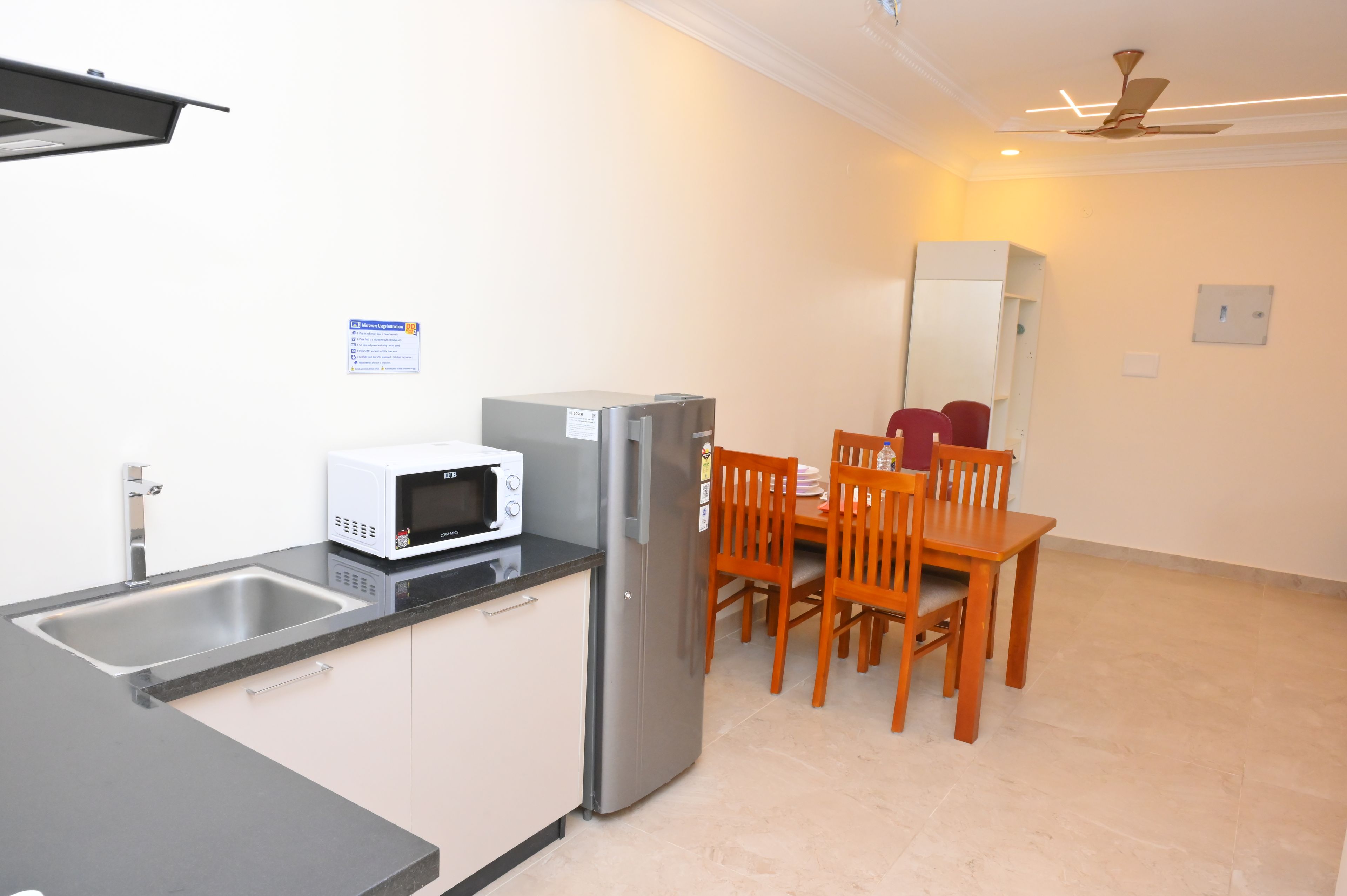 Una cocina compacta con microondas, refrigerador y un comedor con sillas y mesa.