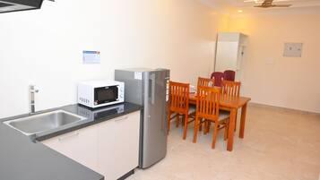 Una cocina compacta con microondas, refrigerador y un comedor con sillas y mesa.